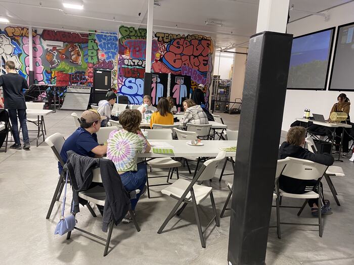 A class in progress at the tables, with the graffiti wall and screens behind