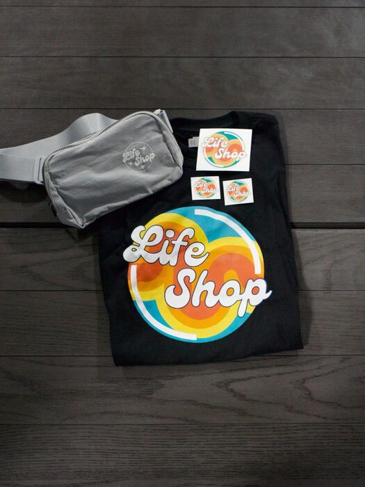 A Life Shop tee, belt bag and stickers laid out together