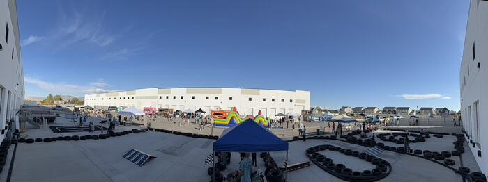 A panorama of a Life Shop outdoor event: the ramp park on one side, a tyre-lined crazy cart circuit on the other, food trucks and bounce houses behind