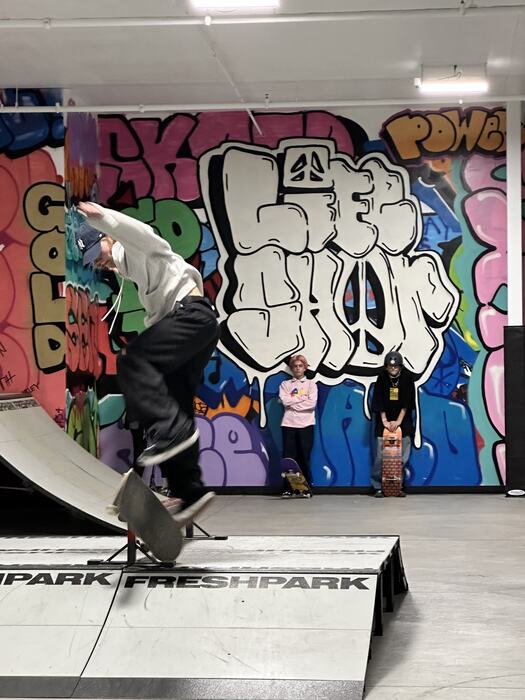A teen mid-trick on the ramp in front of the LIFE SHOP throw-up