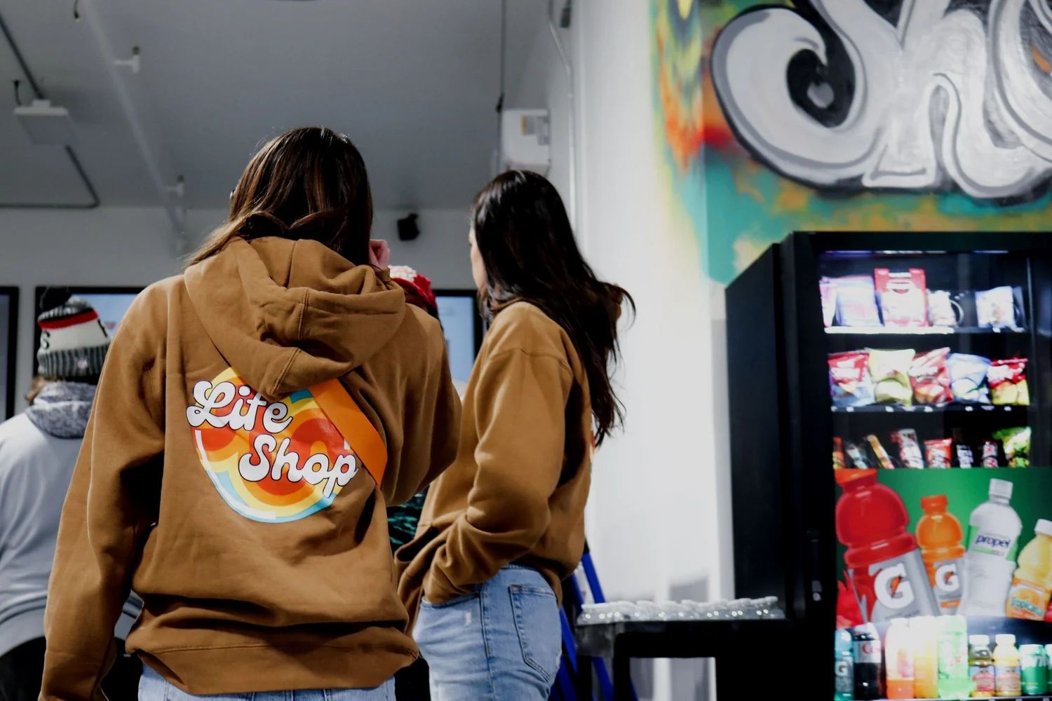 Two teenagers in Life Shop hoodies beside the snack fridge at Life Shop